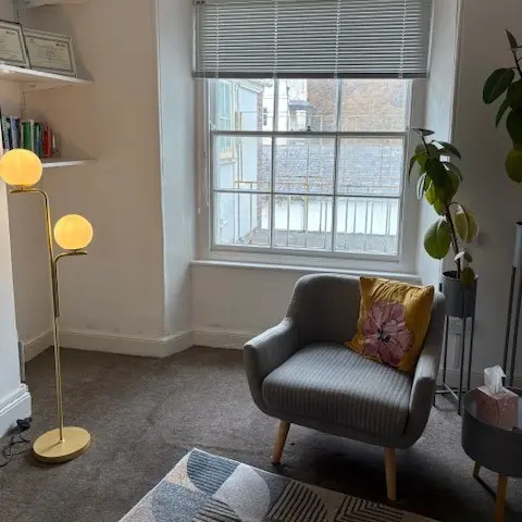 Armchair by the window in Alicia’s counselling room, with a soft lamp and plants